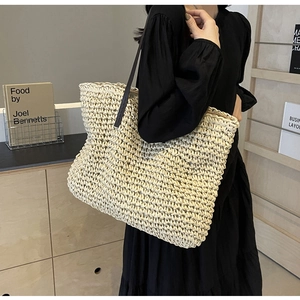 Macro view of large woven straw tote bag texture and long black leather shoulder strap