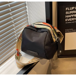 Detail of black shell crossbody bag featuring a wide jacquard floral shoulder strap