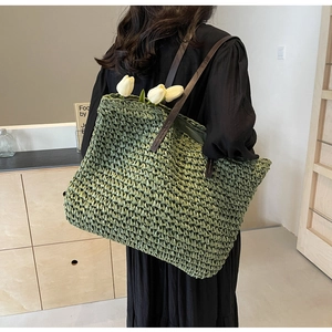 Close-up of green woven straw tote bag featuring brown leather handles and tulip detail