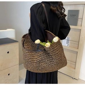 Close-up of a large brown straw tote bag featuring fine weaving and long leather shoulder straps