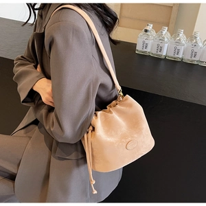 Close-up of beige velvet bucket bag with drawstring and tassel details on grey blazer