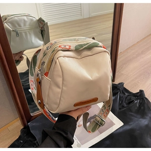 Detail of off-white shell bag with colorful embroidered strap and silver-tone zippers