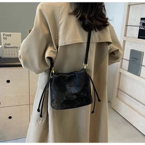 Detailed view of black bucket bag with drawstring closure on model in beige trench coat