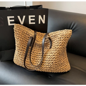 Close-up of a woven straw tote bag with brown leather handles on a black leather sofa