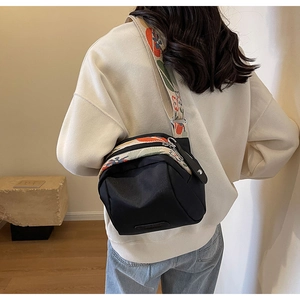 Detail of black canvas crossbody bag featuring colorful floral embroidered wide strap