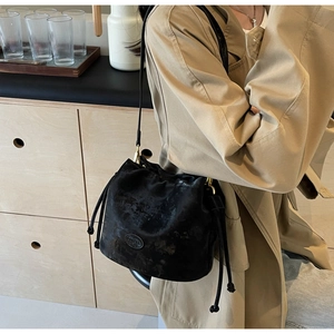 Detail of black drawstring bucket bag showing matte texture and gold metal accents
