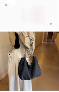 Vue latérale du grand sac cabas en denim noir avec chaîne argentée porté par un mannequin