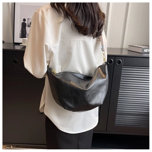 Detail of black Hobo crossbody bag with a patterned wide strap worn by a model