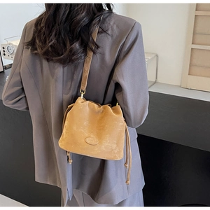 Back view of a model wearing a tan suede drawstring bucket bag with CASHEW logo patch