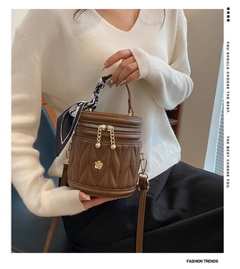Detail of dark brown bucket bag featuring vertical quilted texture and silk scarf handle