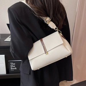 Elegant cream textured leather crossbody bag with wide strap worn by a woman in a suit