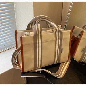 Détail du cabas en toile beige avec garniture en cuir marron et bandoulière rayée