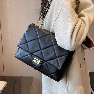 Quilted black leather shoulder bag with gold chain strap worn by a model in a warm room