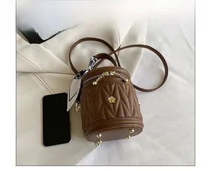 Brown quilted bucket bag with silk scarf handle and gold flower charm on white suit