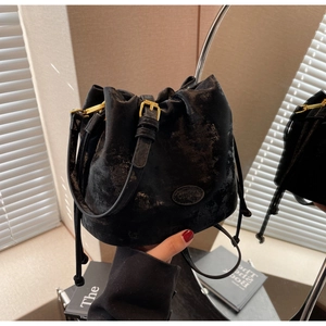 Detail of black drawstring bucket bag showing matte textured leather and golden hardware