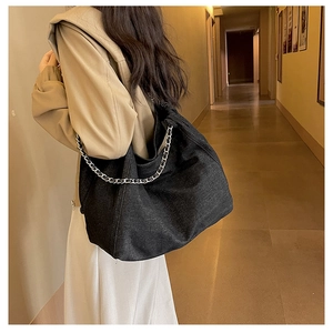 Détail d'un grand sac hobo en denim noir avec bandoulière chaîne argentée à l'épaule
