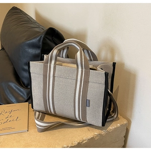 Détail du cabas en toile beige avec bandoulière rayée et finitions en cuir sur pierre
