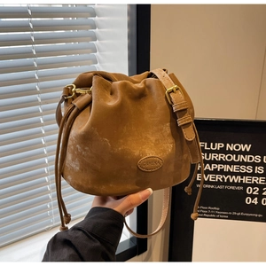 Close-up of brown suede bucket bag with C&HEKA leather patch and gold hardware