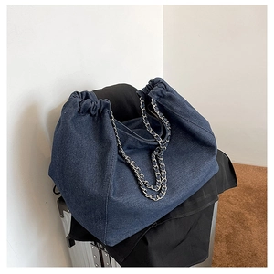 Détail du sac en denim bleu avec fermeture à cordon et bandoulière chaîne en métal