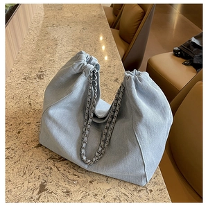 Détail du sac cabas en jean bleu clair avec bandoulière chaîne et cordon serrage