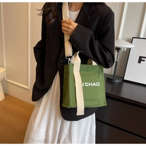 Detailansicht der grünen Canvas-Eimertasche mit breitem cremefarbenem Stoffriemen am Modell