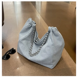 Détail d'un sac fourre-tout en denim bleu clair avec chaîne argentée et cordon de serrage