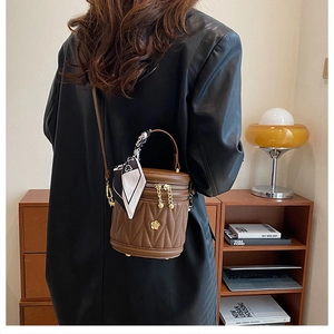 Detail of a brown quilted bucket bag with gold flower hardware and a silk scarf handle
