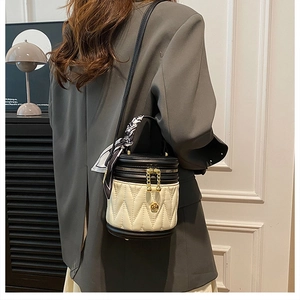 Detail of a black and white quilted bucket bag with gold flower charm and silk scarf decoration