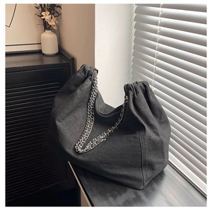 Détail d'un sac cabas en denim noir avec bandoulières en chaîne argentée au décor minimaliste