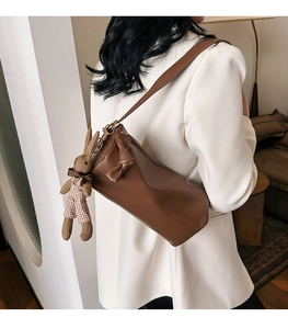 Detail view of a brown cylinder crossbody bag featuring a cute knit bunny pendant