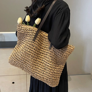 Large straw woven tote bag with brown leather straps shown on shoulder for beach or vacation