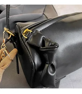Detail of a black cylinder bag with side bow decoration and golden metal hardware zipper