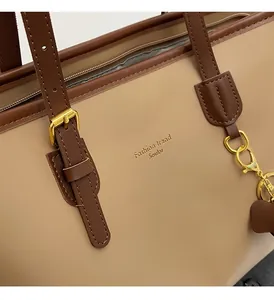 Detail of beige tote bag showing golden zipper and brown leather shoulder strap joint