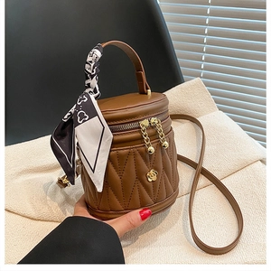 Detailed view of a brown leather bucket bag with vertical quilting and a floral gold charm