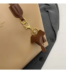 Detail of a dark brown elephant leather charm attached to a tan tote bag with golden clasp
