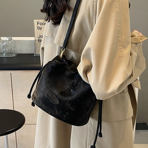 Chic black drawstring bucket bag in vintage frosted leather worn with a beige trench coat