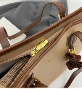 Close-up of smooth gold metal zipper and brand logo on a beige leather tote bag