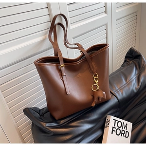 Detail of deep brown leather tote bag with elephant charm and gold hardware accents