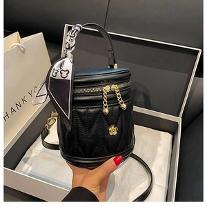 Detailed close-up of a black quilted bucket bag with golden flower logo and silk scarf