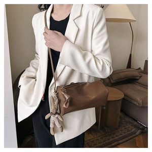 Brown leather cylinder bag with side bow detail and plush rabbit charm on model