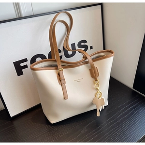 Detail of cream tote bag with brown trim, logo print and cute elephant charm accessory