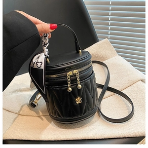 Detail of black quilted mini bucket bag with gold flower charm and silk scarf handle