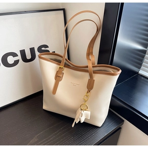 Detail of minimalist cream tote bag with adjustable brown strap and elephant charm