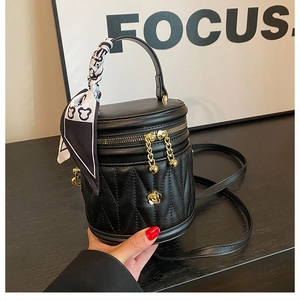 Detail of black quilted bucket bag with golden floral hardware and printed silk scarf handle