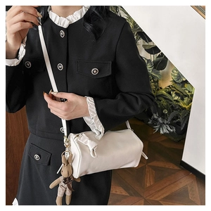 Detail of white cylindrical crossbody bag featuring a leather bow and cute bunny pendant
