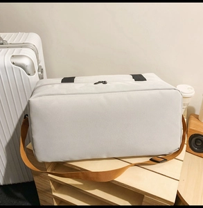 Detail der grauen Oxford-Reisetasche mit braunem Gurt auf einem Holztablett