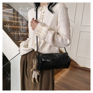 Detail of black cylindrical crossbody bag with bow accent and rabbit plush charm