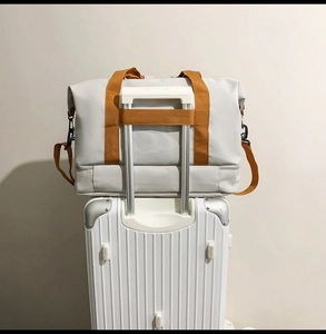 Graue Reisetasche mit orangen Riemen und Trolley-Hülle am Koffer-Detail