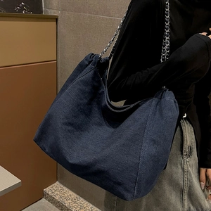 Grand sac cabas en denim bleu foncé avec chaîne en argent porté par un mannequin femme