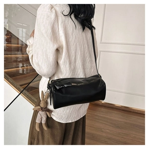 Detail of black leather barrel bag with a plaid rabbit charm worn over the shoulder